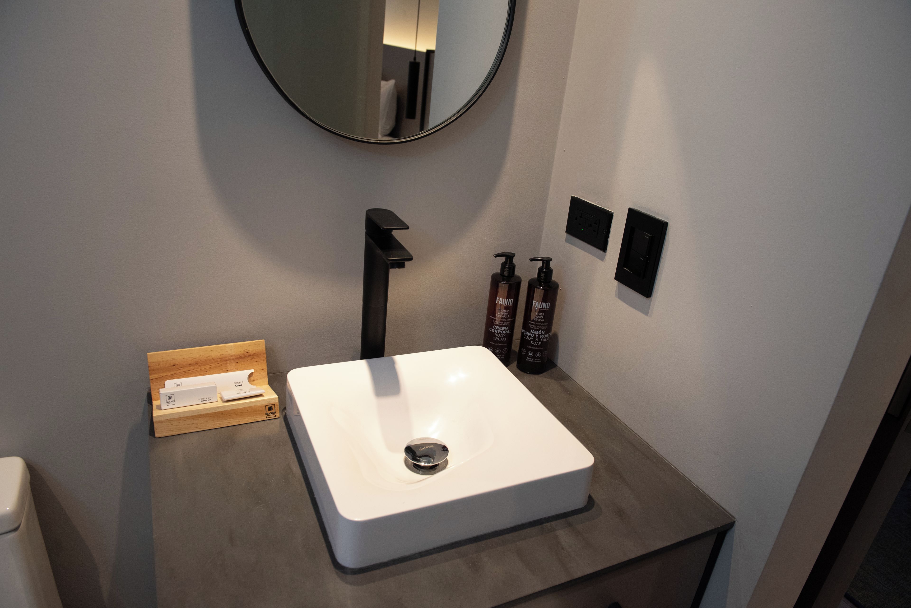 Un baño con lavamanos blanco, un espejo y dos botellas de champú.