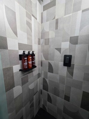 A bathroom with a geometric tile pattern, a black soap dispenser, and a shelf with three bottles of shampoo. - BLOSS HOTEL (Medellín)