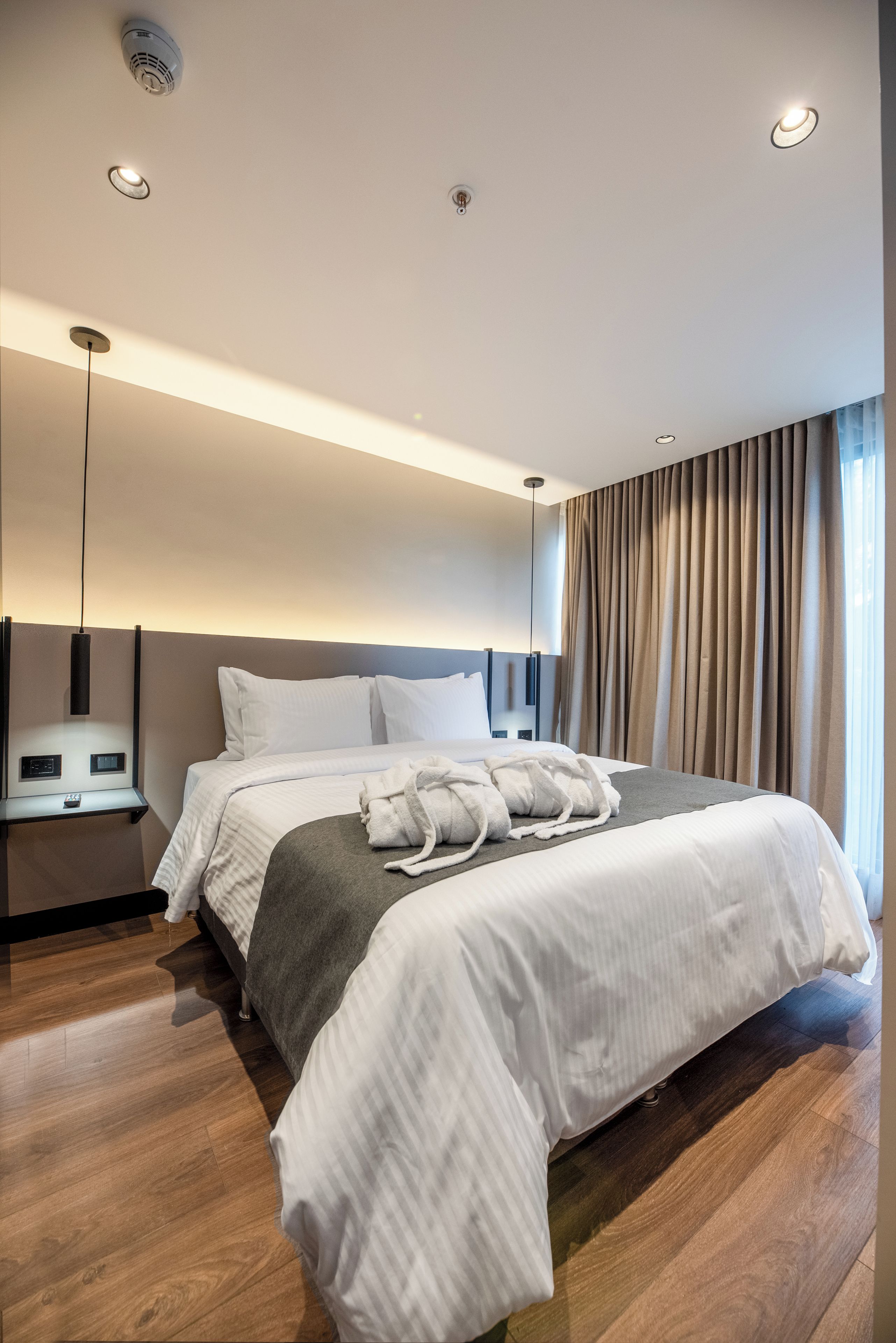 Ein modernes Hotelzimmer mit einem großen Bett, Bedienelementen am Bett, einem Nachttisch und Blick ins Freie durch Vorhänge.