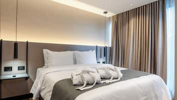 Una habitación de hotel moderna con una cama grande, controles junto a la cama, una mesita de noche y vistas al exterior a través de cortinas.