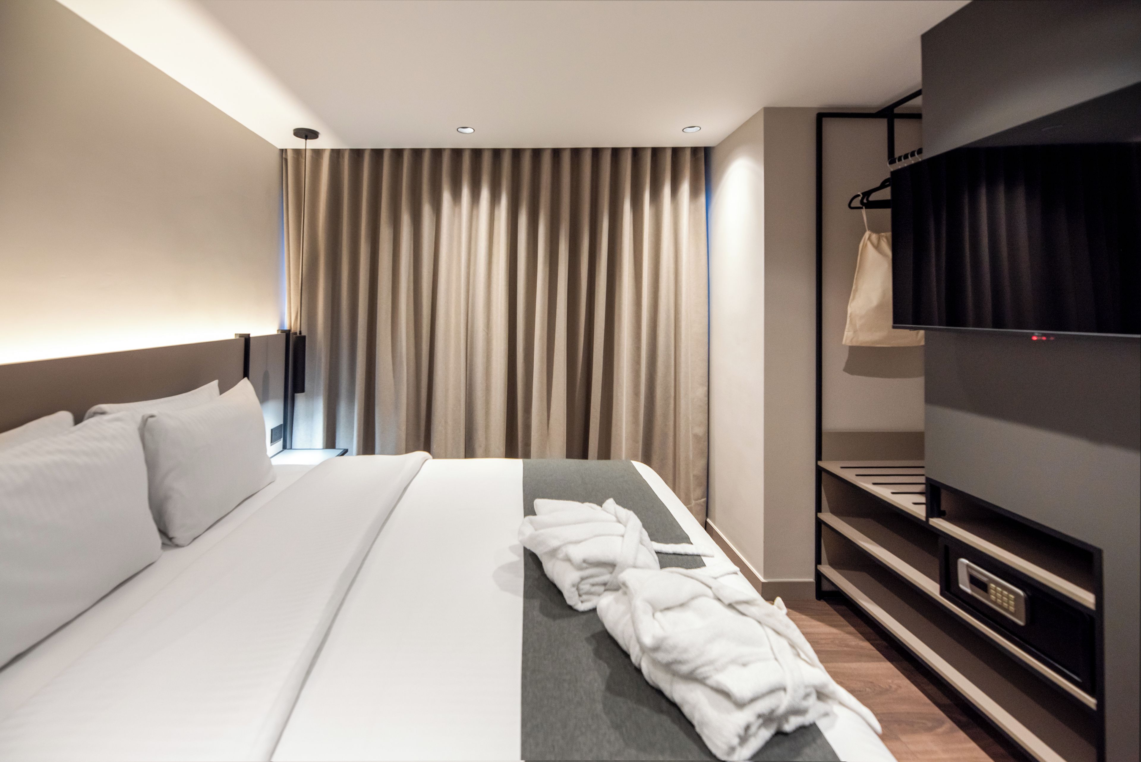 A modern hotel room with a large bed, a flat-screen TV, a wardrobe, and a window with curtains.
