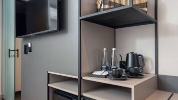 Una habitación moderna con estanterías integradas, un televisor de pantalla plana, cafetera y lavavajillas compacto.