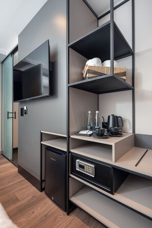 Una habitación moderna con estanterías integradas, un televisor de pantalla plana, cafetera y lavavajillas compacto.