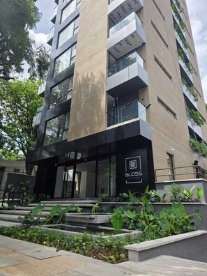 A modern hotel building with a prominent logo, large windows, and a landscaped entrance area. - BLOSS HOTEL (Medellín)