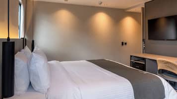 Una habitación de hotel moderna con una cama grande, un escritorio y un televisor de pantalla plana.