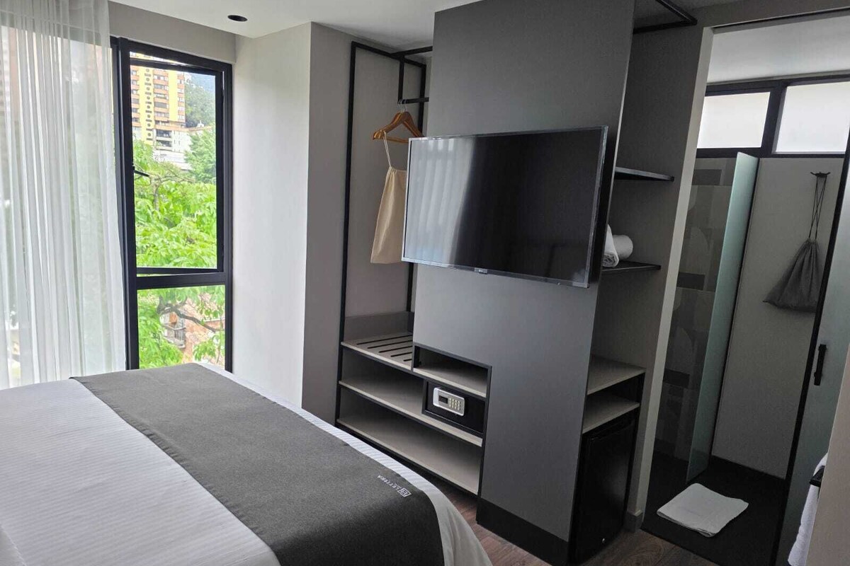 A modern hotel room with a bed, a TV, a wardrobe, and a shower area.