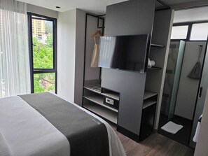 A modern hotel room with a bed, a TV, a wardrobe, and a shower area. - BLOSS HOTEL (Medellín)