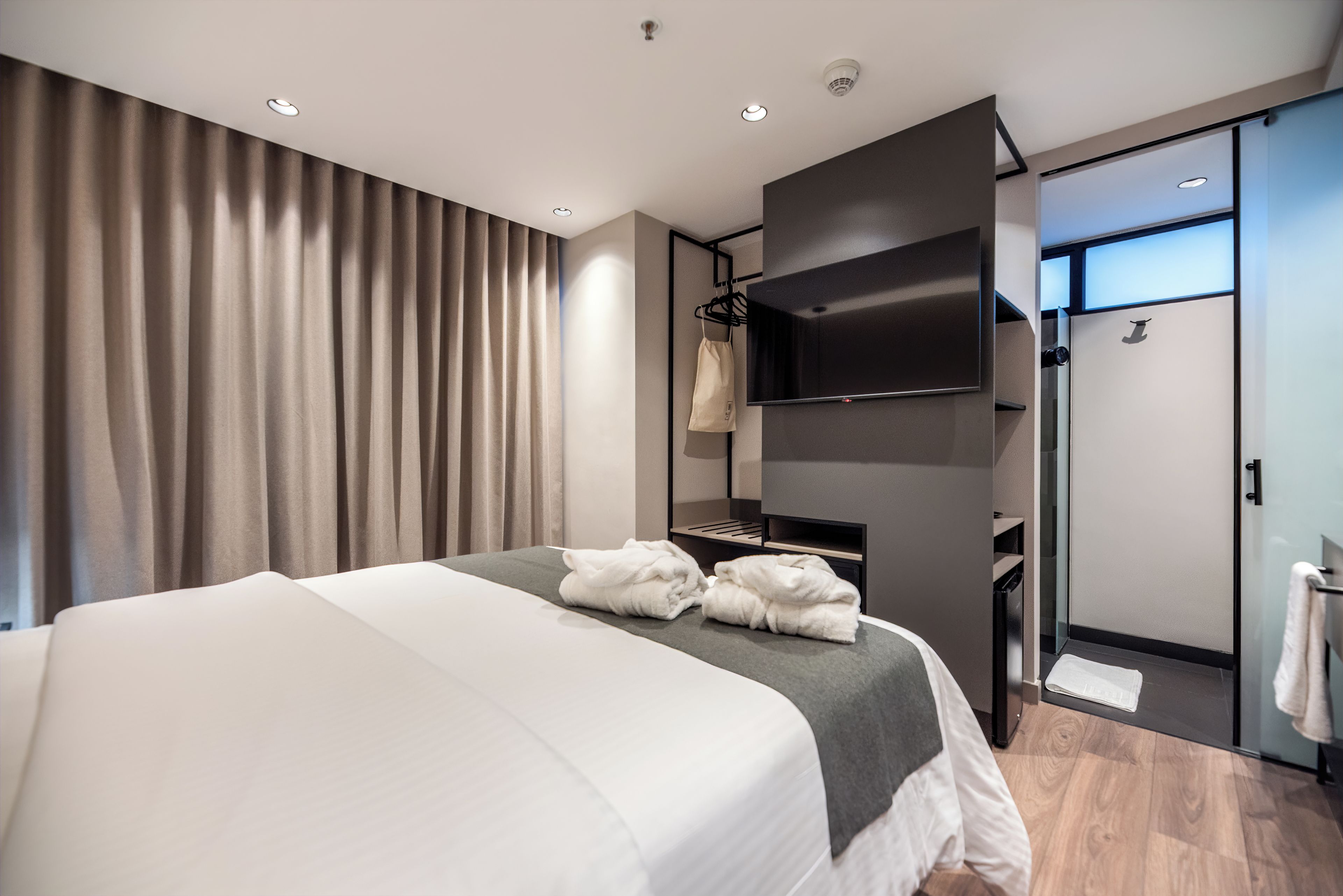 A modern hotel room with a large bed, a flat-screen TV, a shower area, and a wardrobe.