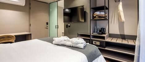 A modern hotel room with a large bed, a flat-screen TV, a wardrobe, and a seating area with a chair.