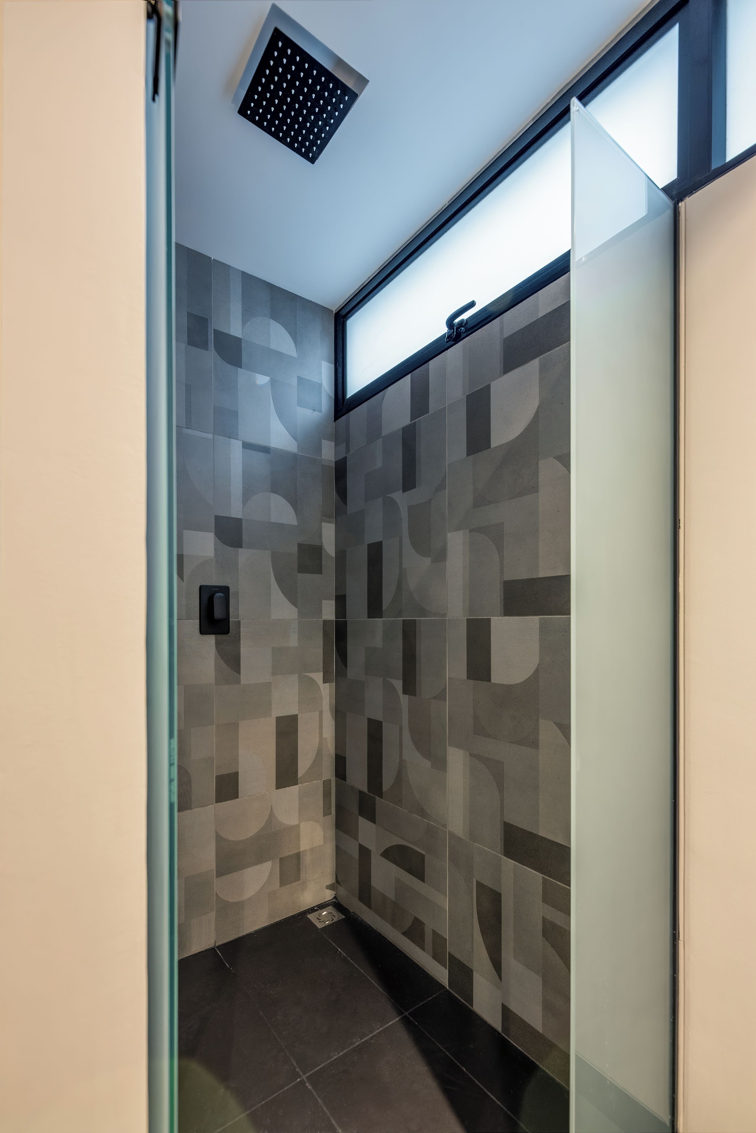A modern shower with a geometric tile pattern, a glass door, and a ceiling-mounted showerhead.