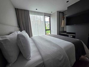 A modern hotel room with a large bed, a flat-screen TV mounted on the wall, and a window with curtains. - BLOSS HOTEL (Medellín)