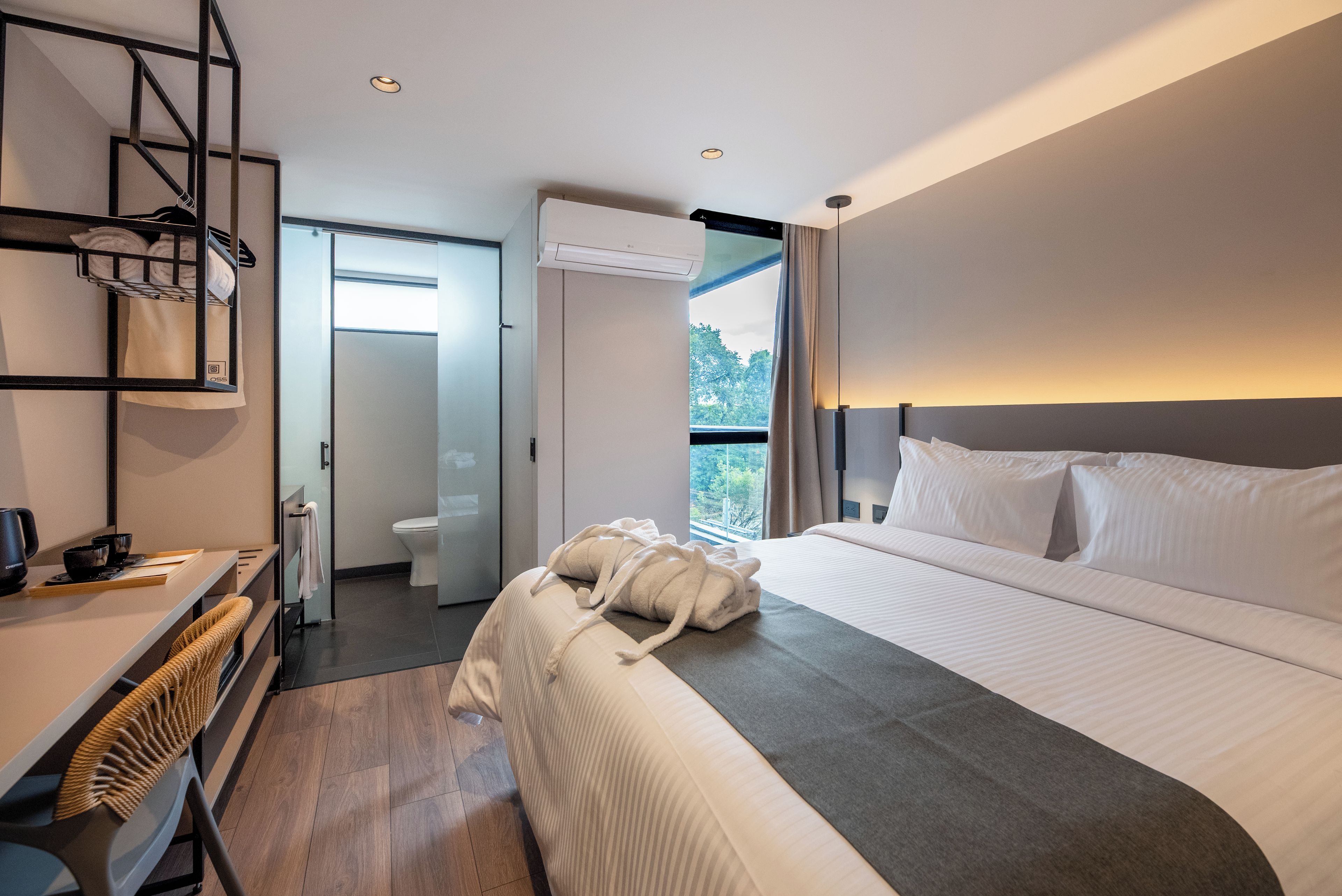 Habitación de hotel moderna con una cama grande, un escritorio con hervidor y vistas al exterior.