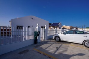 A parking area with a white car, a gated entrance, and a building with a blue roof. - Aruba Vibe Apartments 8 | Charming Studio Near the Beaches and Downtown (Oranjestad)