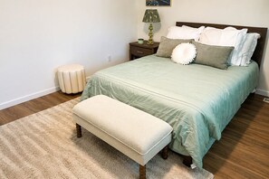 Ein Schlafzimmer mit einem Bett, einer Bank, einem Nachttisch, einer Lampe und einem kleinen Hocker.