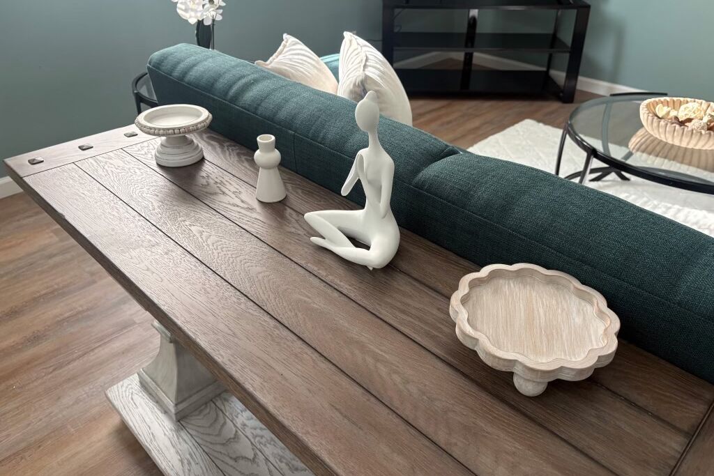 A modern living room with a wooden coffee table, a green sofa, and decorative items including a white ceramic sculpture and a small wooden bowl.
