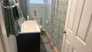 Ein Badezimmer mit einem weißen Waschbecken, einer Toilette, einer Duschkabine und einem grünen Handtuchhalter.