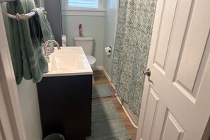 A bathroom with a white sink, a toilet, a shower curtain, and a green towel rack. - The Gem On The Block (Springfield)