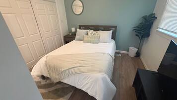 A bedroom with a bed, bedside table, lamp, and a potted plant.