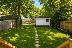 Ein Garten mit Rasen, Holzzaun, Gartenhaus und Bäumen.