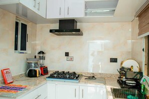 Une cuisine avec des meubles blancs, une cuisinière à gaz, un mixeur et un égouttoir à vaisselle.
