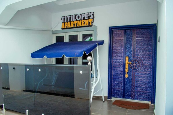 En entré med ett blått markis, en skylt med texten ”TITILOPE’S APARTMENT” och en blå dörr med ett nyckelhål.