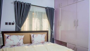 A bedroom with a bed, curtains, a wardrobe, and a window with a view. - The Haven | Modern 2BR En-suite Flat (Ibadan)