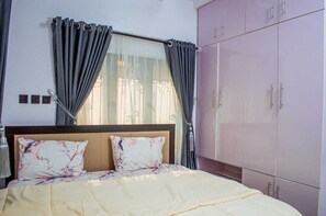 A bedroom with a bed, curtains, a wardrobe, and a window with a view. - The Haven | Modern 2BR En-suite Flat (Ibadan)