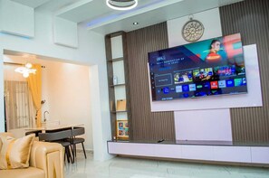 A modern living room with a flat-screen TV mounted on the wall, a dining area with a table and chairs, and a sofa. - The Haven | Modern 2BR En-suite Flat (Ibadan)