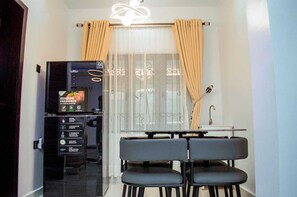 A modern living room with a dining area, featuring a digital refrigerator, a dining table with chairs, and a large window with curtains. - The Haven | Modern 2BR En-suite Flat (Ibadan)