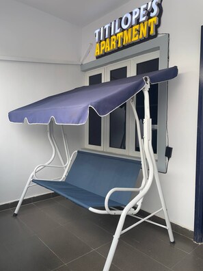 A waiting area with a blue bench and a canopy, a window, and a sign reading 'TITILOPE'S APARTMENT'. - The Haven | Modern 2BR En-suite Flat (Ibadan)