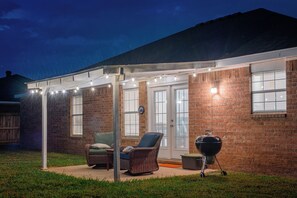 A covered patio with wicker furniture, a barbecue grill, and string lights. - Quiet 3-Bedroom Home Convenient to Everything Northwest Arkansas has to Offer (Centerton)