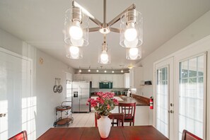 Una cocina moderna con armarios blancos, un refrigerador de acero inoxidable y una zona de comedor con mesa y sillas de madera.