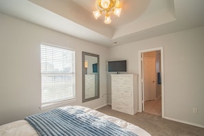 Un dormitorio con cama, cómoda, televisor y puerta que da a otra habitación.