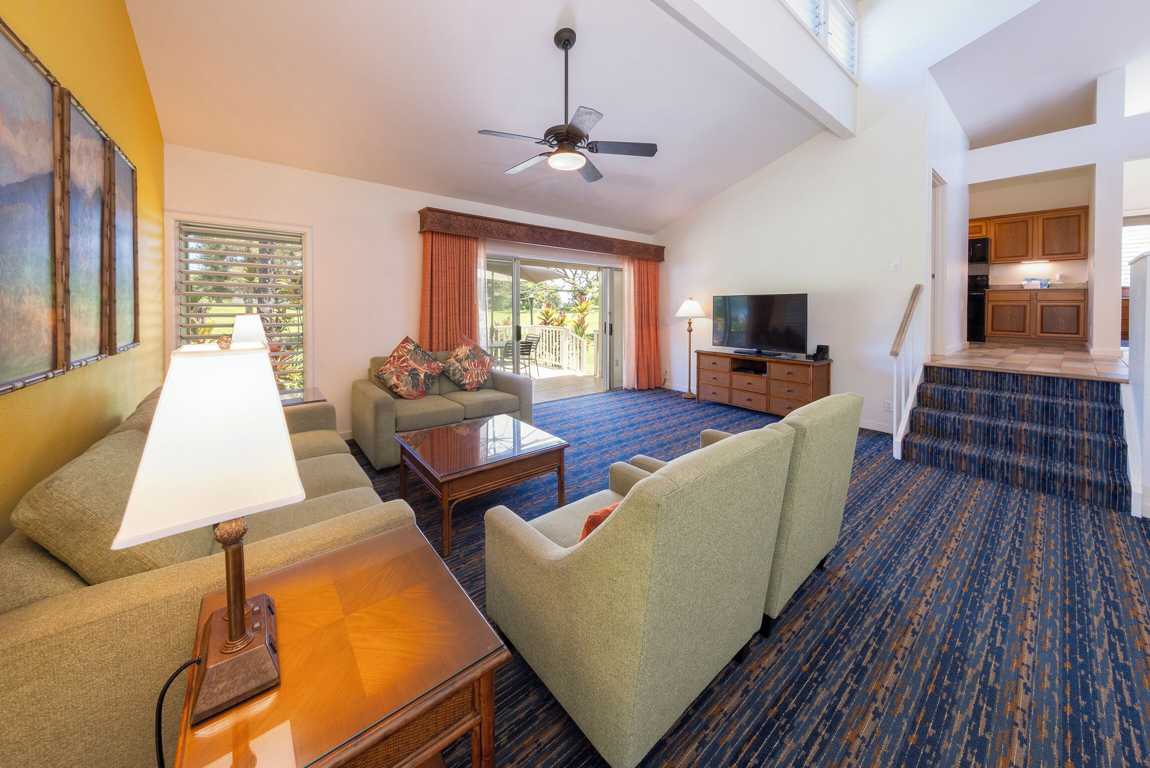 A hotel room with a sofa, a coffee table, a television, a dining area, and a staircase leading to the kitchen.