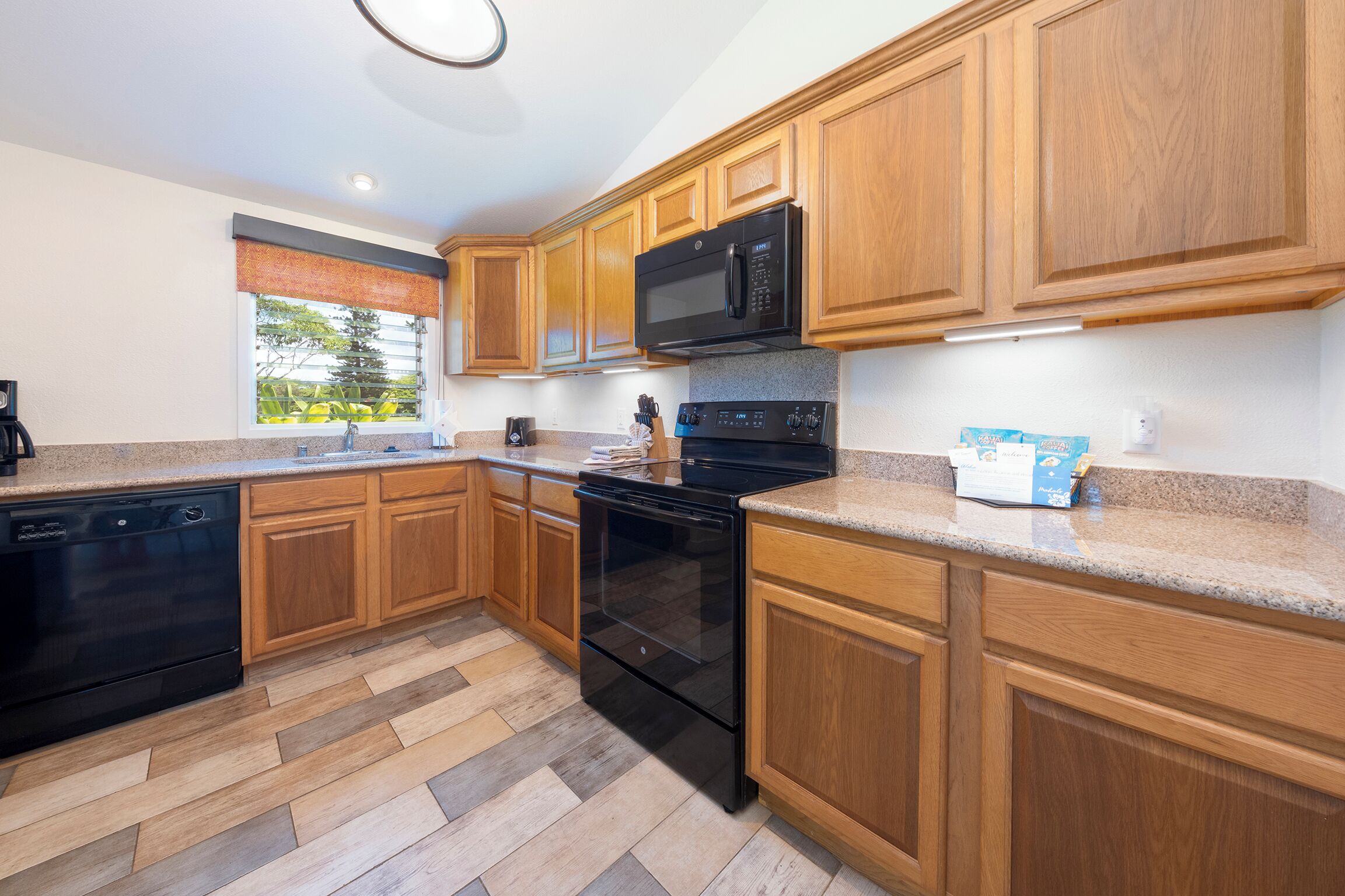 A modern kitchen with wooden cabinets, a black microwave, and a stainless steel oven.