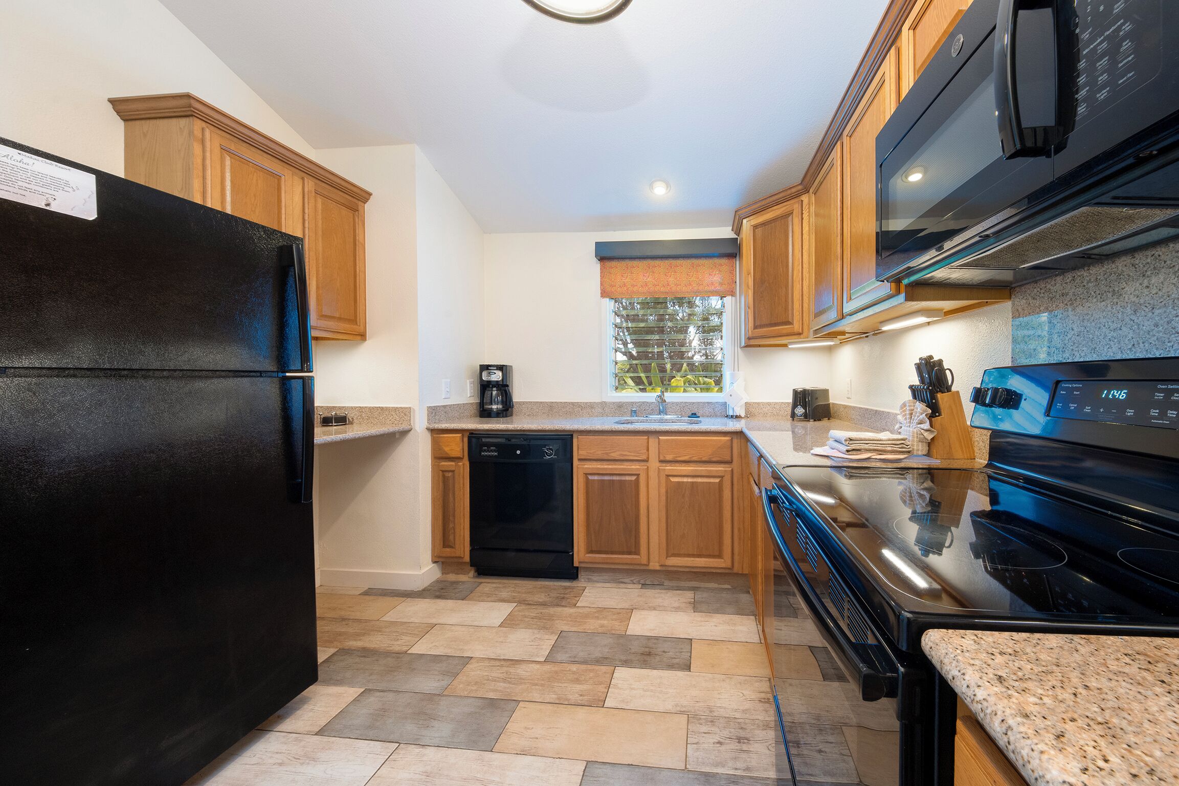 A modern kitchen with a black refrigerator, a dishwasher, wooden cabinets, a granite countertop, and a stove.