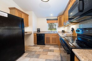 A modern kitchen with a black refrigerator, a dishwasher, wooden cabinets, a granite countertop, and a stove. - The Cottages at Makai Club (Princeville)
