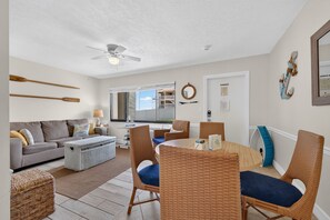 A living room with a sofa, a coffee table, wicker chairs, a ceiling fan, and a view of the outside. - Sun and Sand Getaway @ Coastal Waters (New Smyrna Beach)