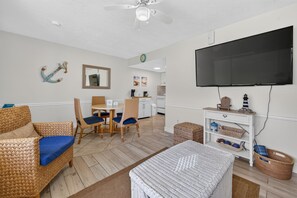 A living room with wicker furniture, a flat-screen TV, and a kitchen in the background. - Sun and Sand Getaway @ Coastal Waters (New Smyrna Beach)