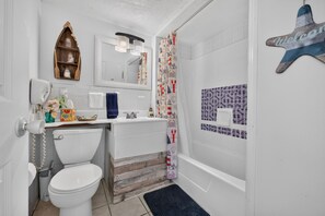 Un baño con inodoro, lavabo y bañera. Hay un estante de madera sobre el inodoro y una decoración de estrella de mar en la pared.