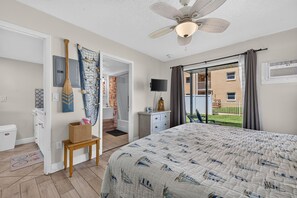 A bedroom with a bed, a ceiling fan, a television, and a view of the outside. - Sun and Sand Getaway @ Coastal Waters (New Smyrna Beach)
