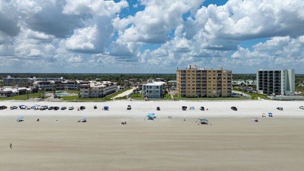 A beachfront hotel with multiple buildings, a sandy beach, and umbrellas. - Sun and Sand Getaway @ Coastal Waters (New Smyrna Beach)