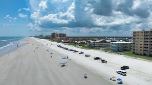 A beach with a row of beach umbrellas and a parking lot with vehicles. - Sun and Sand Getaway @ Coastal Waters (New Smyrna Beach)