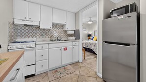 A compact kitchen with white cabinets, a stainless steel refrigerator, and a gas stove. - Sun and Sand Getaway @ Coastal Waters (New Smyrna Beach)