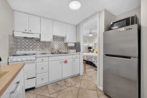A compact kitchen with white cabinets, a stainless steel refrigerator, and a gas stove. - Sun and Sand Getaway @ Coastal Waters (New Smyrna Beach)