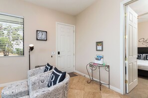 A room with a bed, a chair with a pillow, a clock, a door, and a small table with a book and a bottle. - Chateau Blanc Vineyard Estate w/ 7 bedrooms, 5.5 bathrooms, pool, spa, fire pit (Temecula)