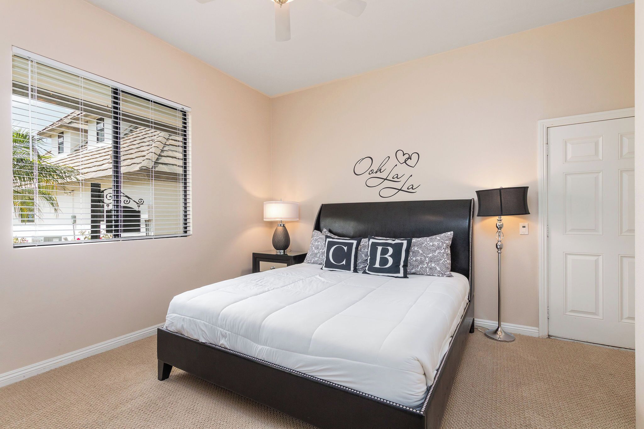 A bedroom with a bed, a nightstand, a lamp, a wall decoration, and a window with blinds.