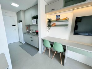 A modern kitchen with white cabinets, a microwave, and a sink. There are two green chairs at a white table.