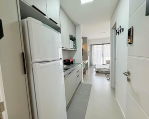 A compact kitchen with white cabinets, a refrigerator, and a microwave. There is a small dining area with chairs and a table. The room has a neutral color palette and a modern design.