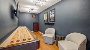A room with a shuffleboard table, two chairs, a dartboard, and wall-mounted artwork. - Henley, Tiny Home Escape with Hot Tub & Fire Pit in Fredericksburg (Fredericksburg)